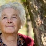 elderly woman standing by tree looking toward the sky