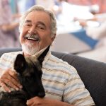 elderly man sitting in chair petting a dog